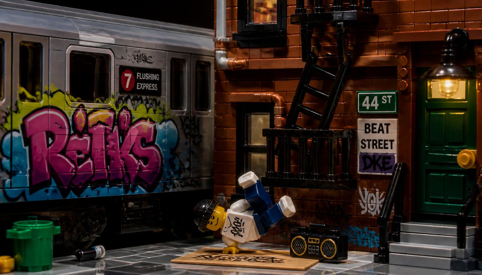 Close-up of a brick-built subway car with graffiti next to a brownstone fire escape and a minifig breakdancer on cardboard